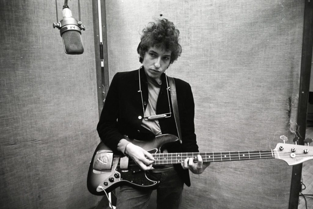 Young Bob Dylan playing a guitar in the studio.