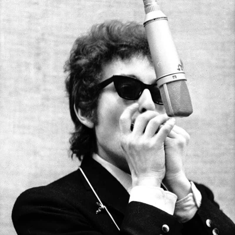 Young Bob Dylan playing harmonica in studio.